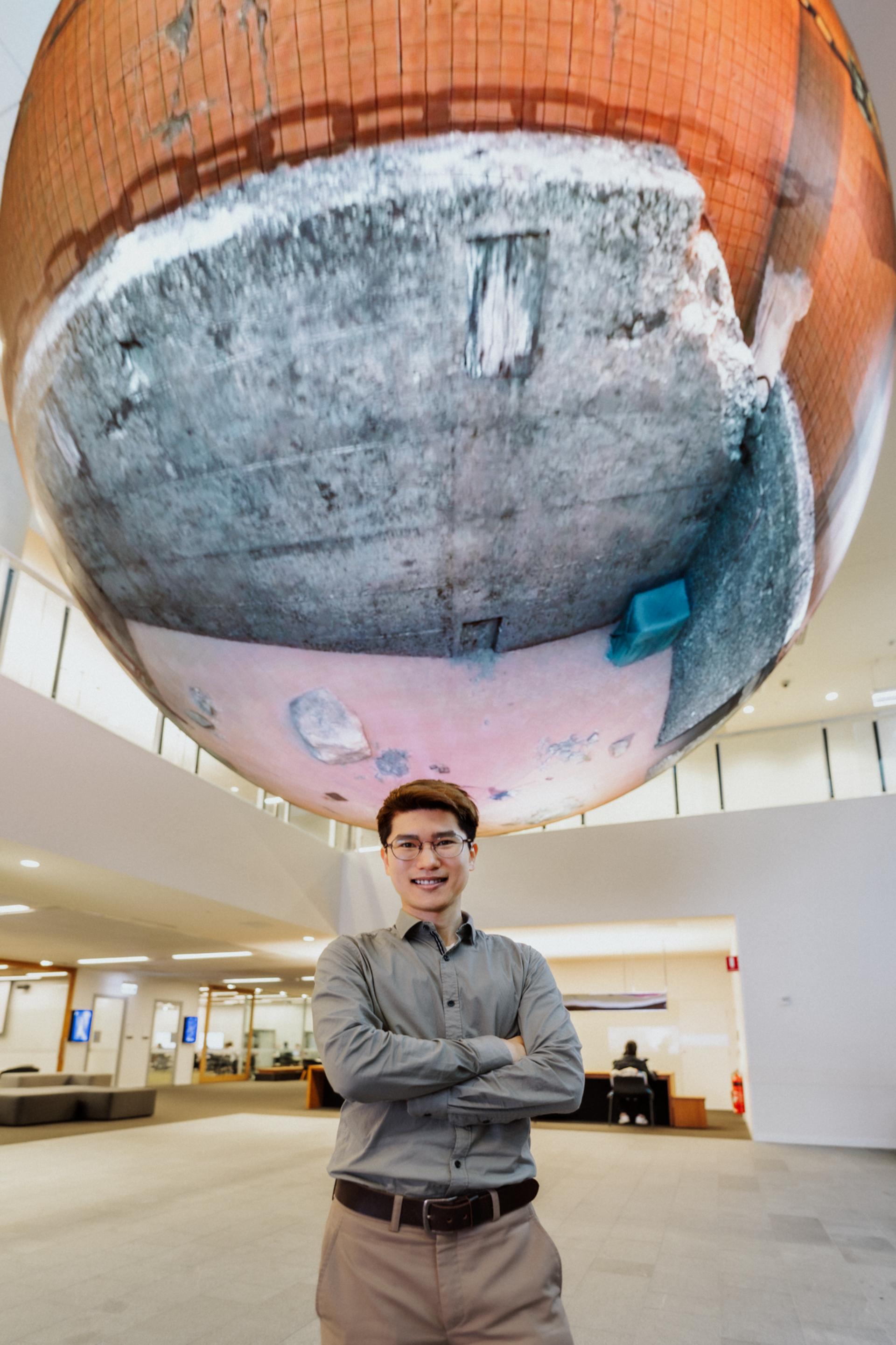 Male student standing under globe feature at QUT in Brisbane. 