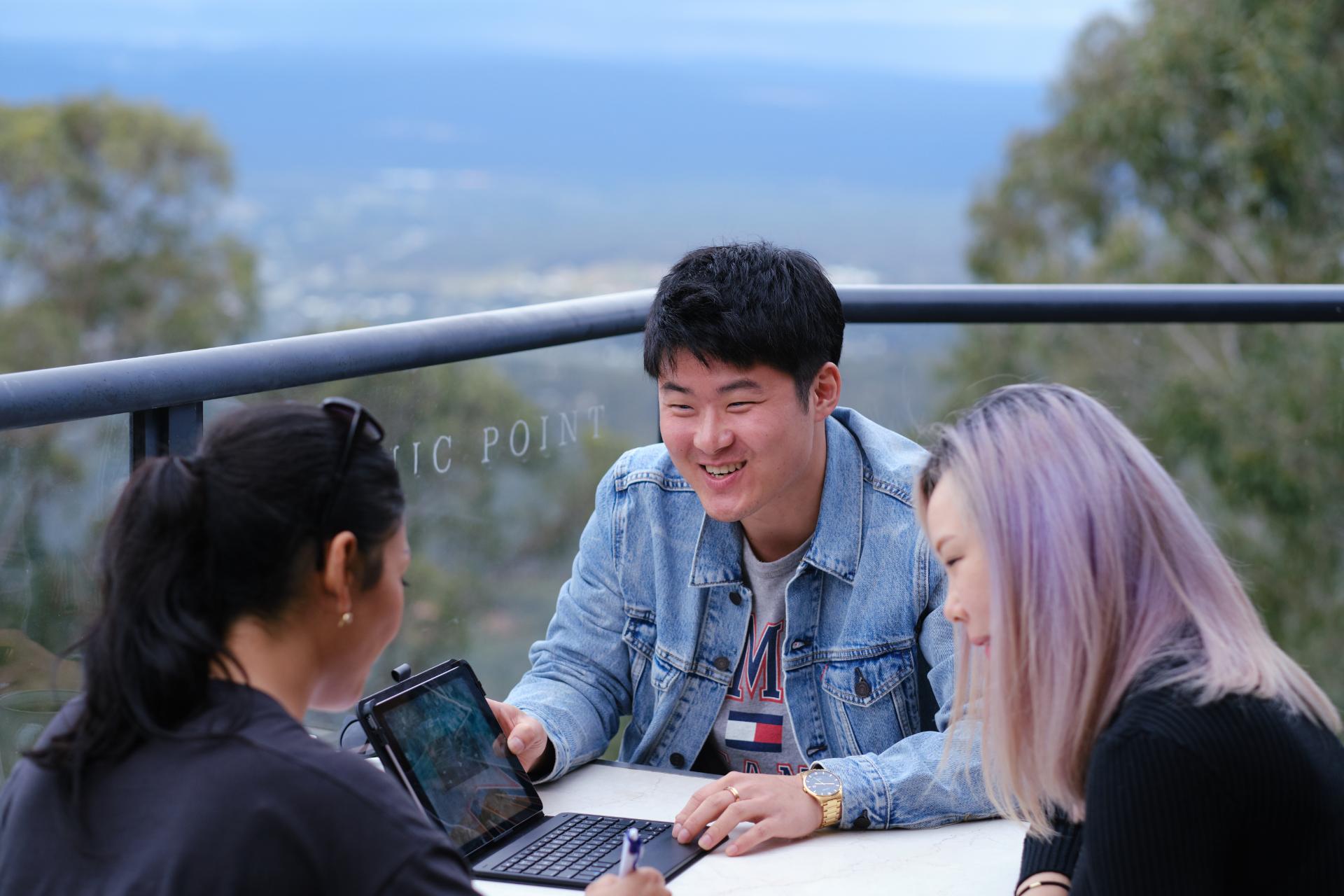 Three students sitting together looking at a laptop. 